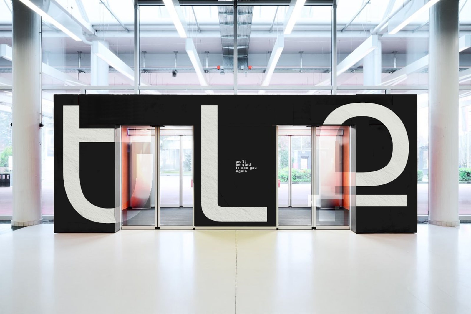 Large-scale environmental signage at a glass-doored building entrance, giant lowercase letterforms.