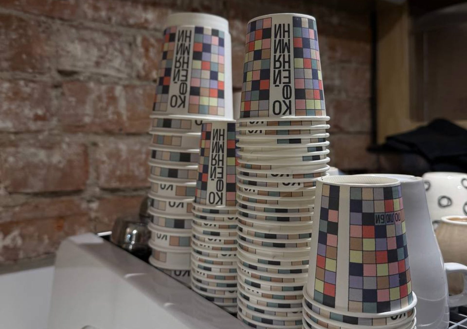 Stacked branded cups, checkerboard pattern and the vertical wordmark wrapping around each one.