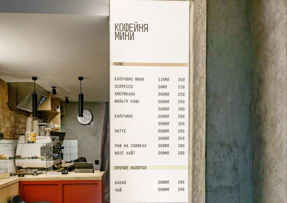 The tall menu board mounted on the room's own narrow column, wordmark at the top, full price list below.