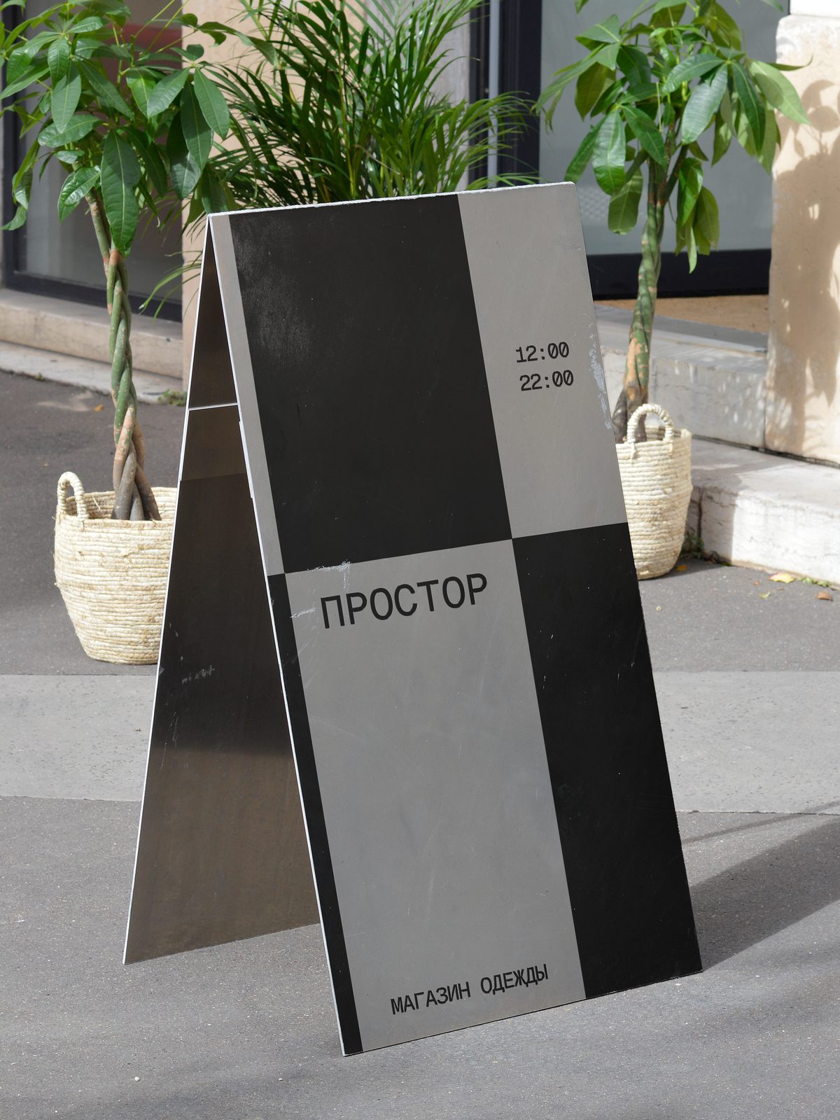 A-frame sidewalk sign outside the store, in black and grey, with hours and address.