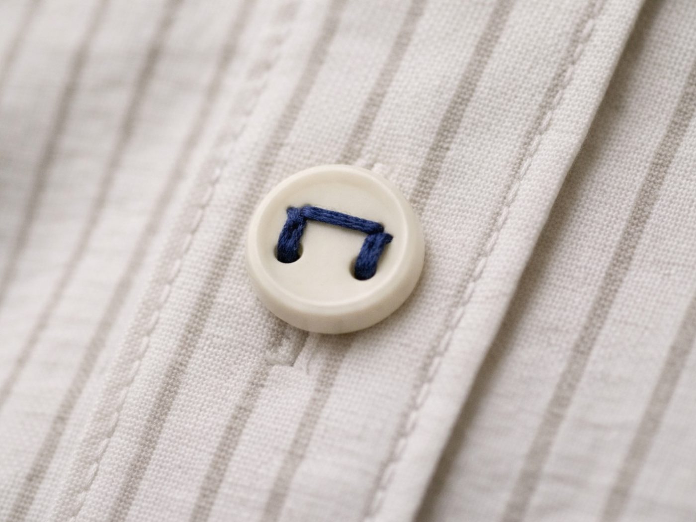 Close-up of a shirt button, with the П mark embroidered in navy thread.