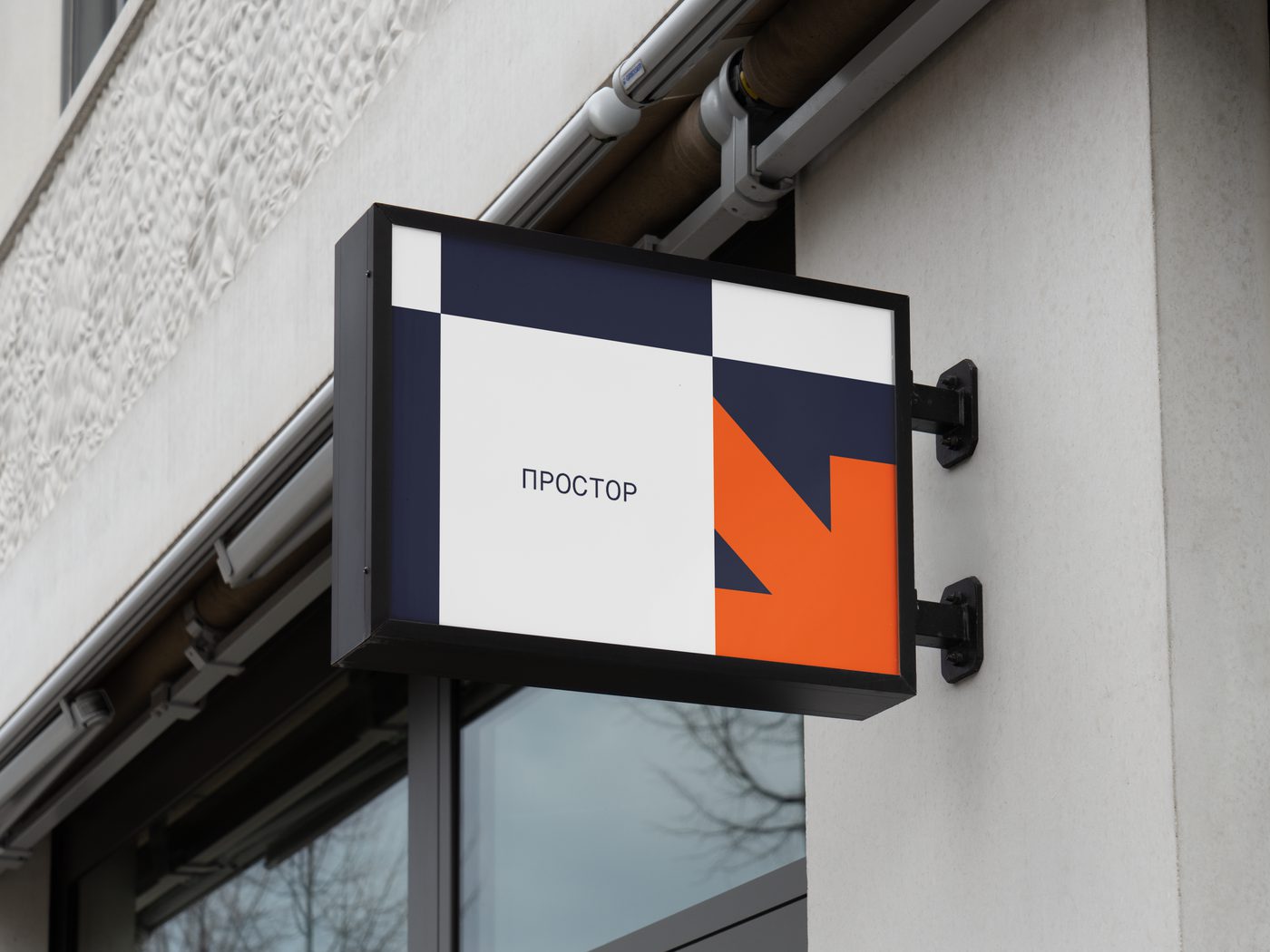 Illuminated wall sign in navy and orange, using the grid mark as a bold directional arrow.